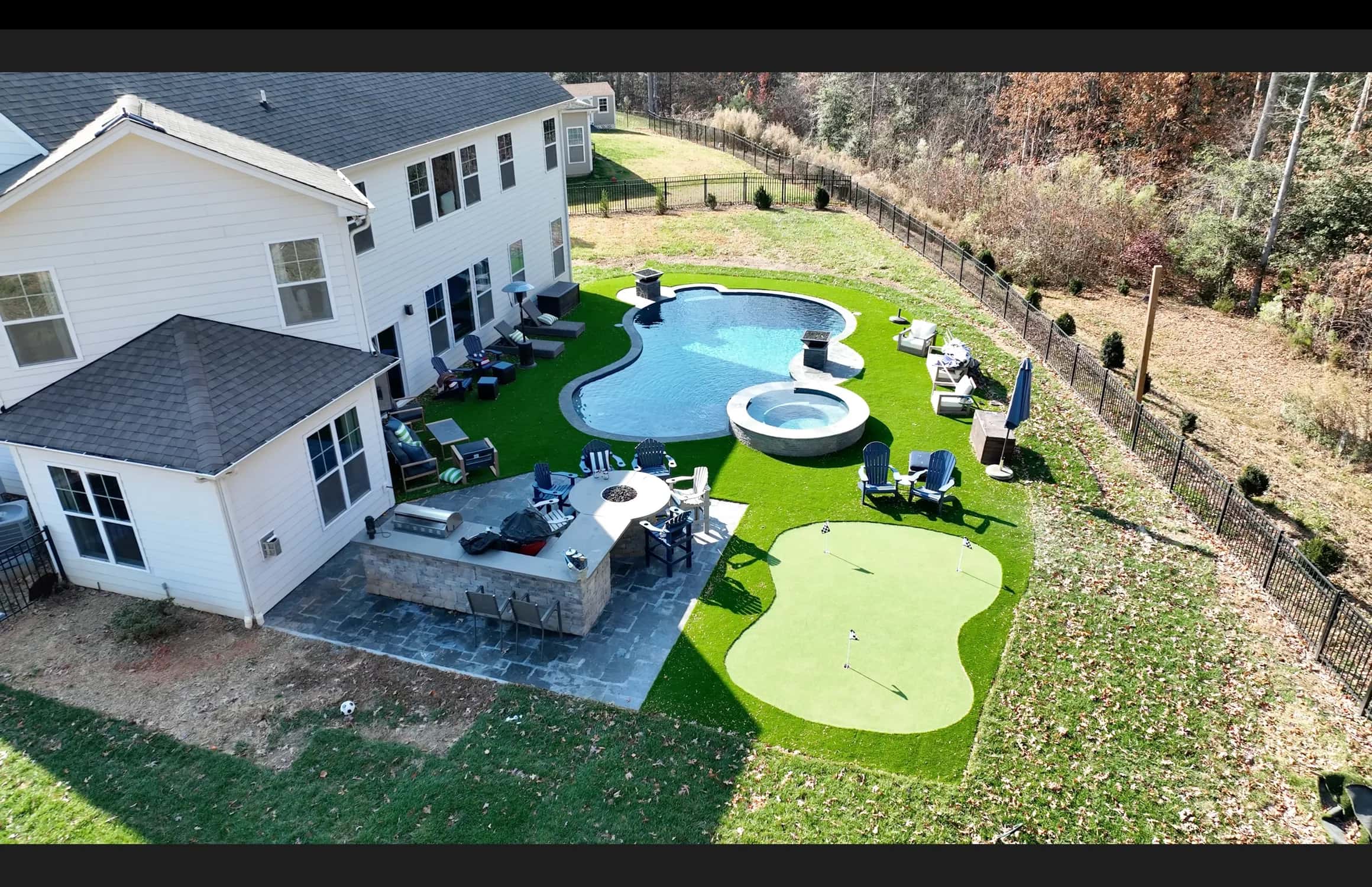 An elevated photograph shows a curved pool, spa, patio and putting green arranged beside a home.