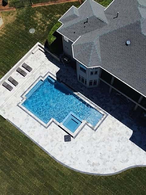 An elevated photograph shows a pool, square spa and surrounding deck beside a house.