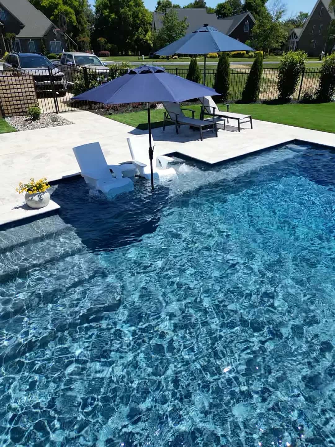 Loungers and umbrellas stand on a pool’s shallow shelf beside deeper water.